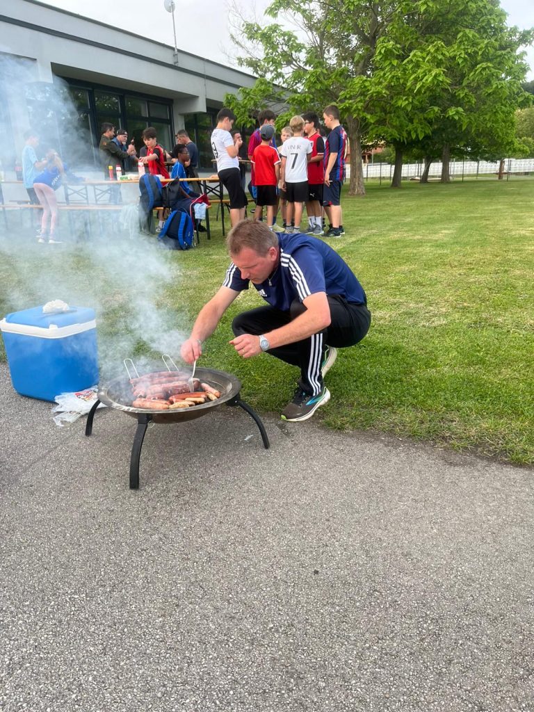Jürgen Schlögl, Trainer der U11 der SPG DER Club, bereitet beim Saisonabschluss Grillwürstel für die Mannschaft und ihre Familien zu. Der gemeinsame Ausklang fand in entspannter Atmosphäre am Sportplatz statt.